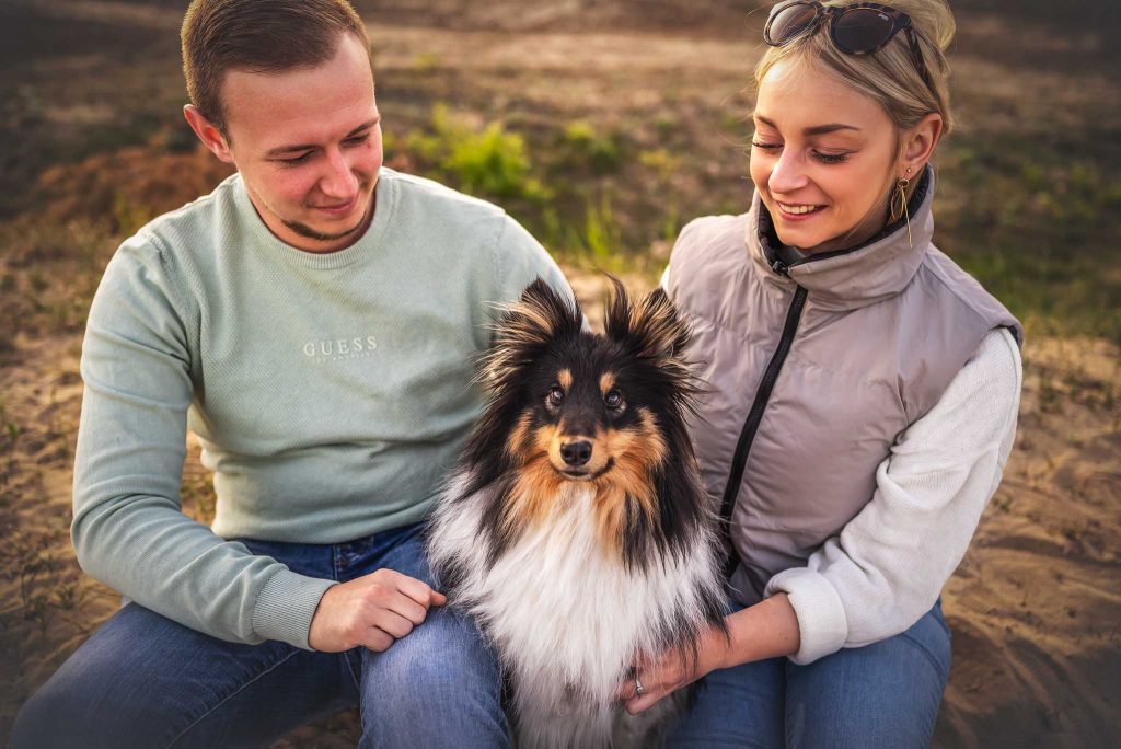 Das Bild zeigt ein junges Pärchen und einen Sheltie Rüden in deren Mitte