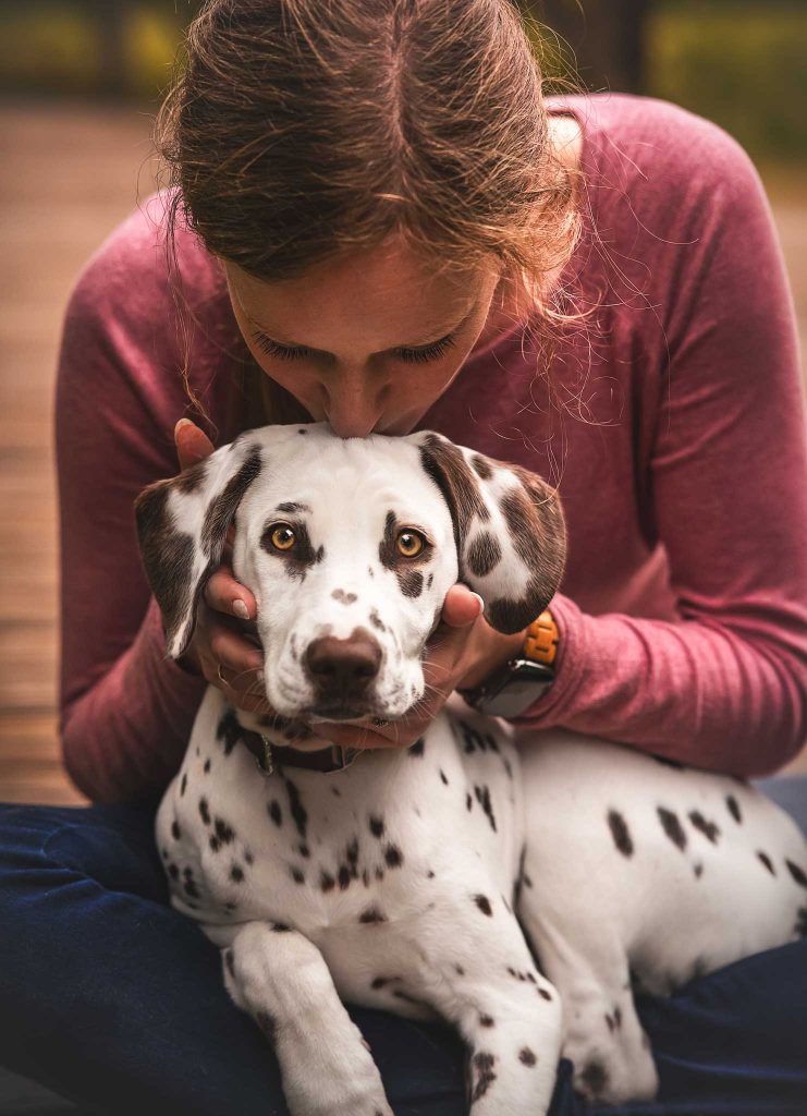 Das Bild zeigt eine junge Frau, die ihrem Welpen einen Kuss auf den Kopf gibt