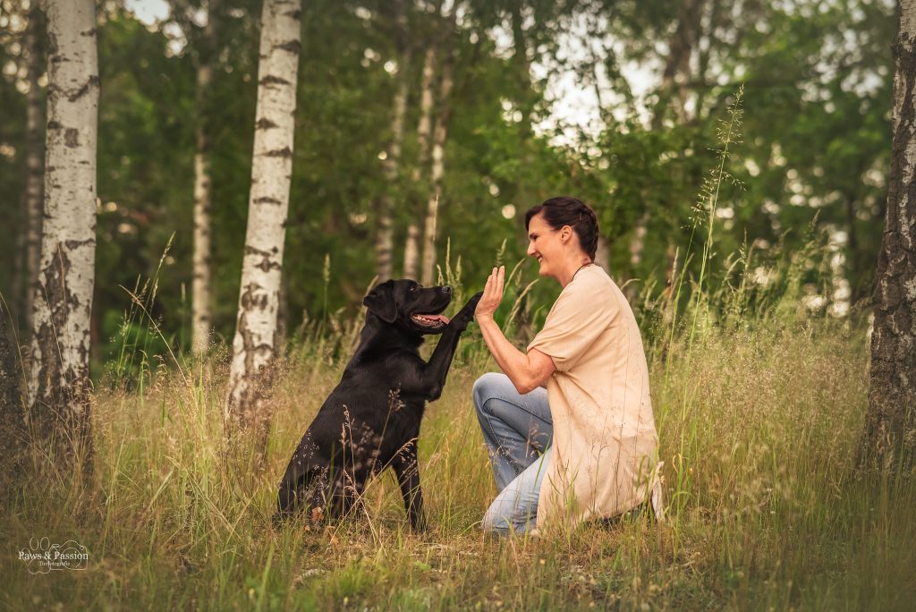 Das Bild zeigt einen Hund, der seiner Besitzerin die Pfote gibt